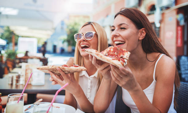 Pizza time. Young girls eating pizza in a cafe. Consumerism, lifestyle stock photo