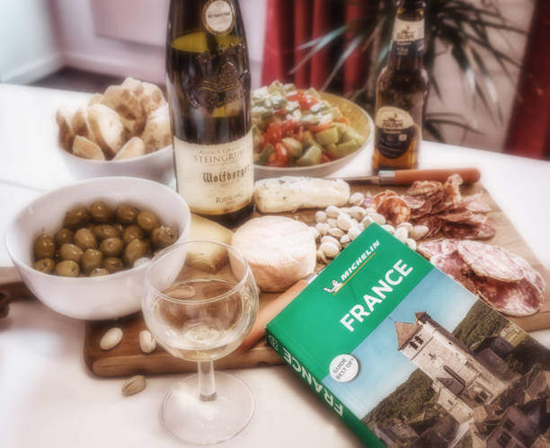 Plan a trip to France with a variety of local products on a cheese board. Colmar, France. MAY 2019 Planning a trip to France with the Michelin Guide book and a wooden board filled with cheese, nuts, bread, olives, Alsace wine and beer. munster france stock pictures, royalty-free photos & images