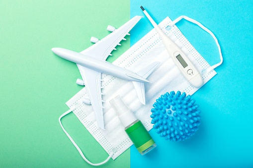 Plane model, thermometer, hand sanitizer and face mask on blue and green background with copy space. International flights after concept of coronavirus (COVID-19).