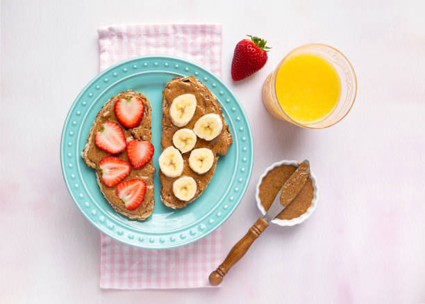Plant based breakfast of whole grain toast, almond butter and fruit Overhead view of whole grain toast with almond butter, strawberries and banana served with orange juice almond butter stock pictures, royalty-free photos & images