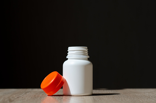 Plastic jar for pills. Cream container. White jar with orange lid. A sterile jar is on the table.