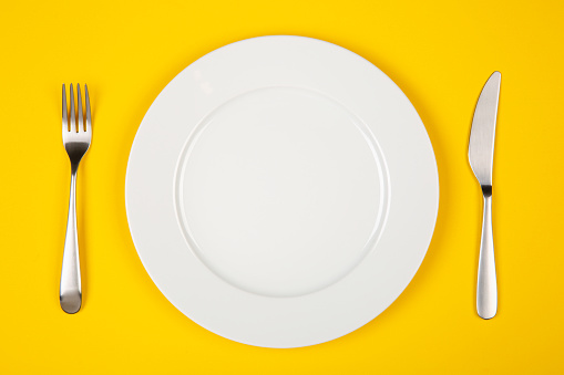 Table setting with white plate, modern cutlery (fork and knife) on yellow table, top view, copy space.