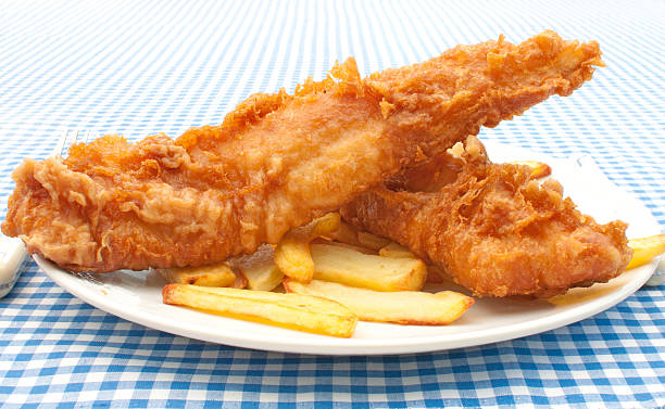 Plate of battered fish and chips on a blue checkered table  Crispy fish fillets with chips on a plate fish fry stock pictures, royalty-free photos & images