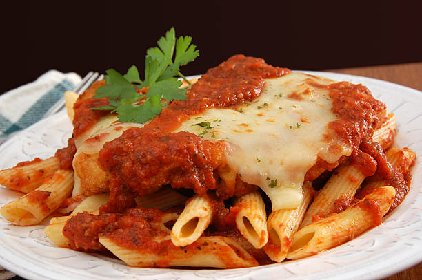 Plate of chicken parmigiana on table garnished with cilantro Italian comfort food - chicken parmigiana served on top of pasta with marinara sauce. parmesan cheese stock pictures, royalty-free photos & images