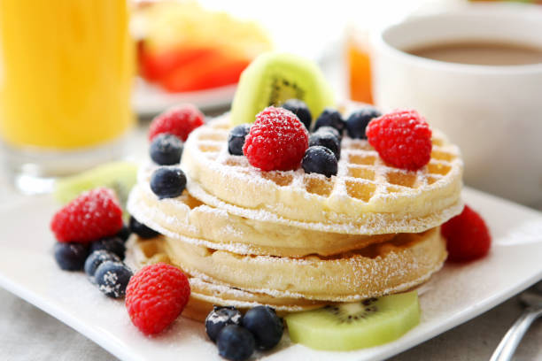 A plate of waffles topped with berries, sugar and kiwi  stock photo
