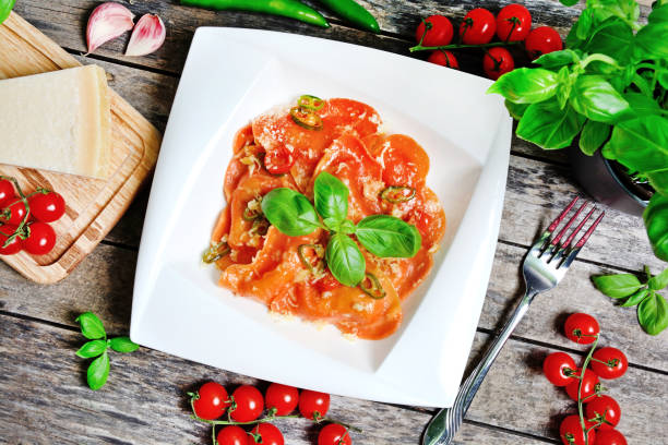 Plate with red heart ravioli with cherry tomato, mozzarella, parmesan and basil on table stock photo