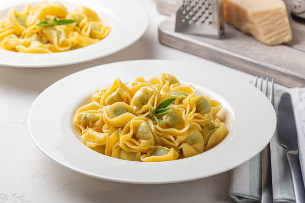 Plates with tortelloni stuffed with spinach and ricotta, stir-fried with melted butter and sage leaves. Parmesan cheese. White background. stock photo