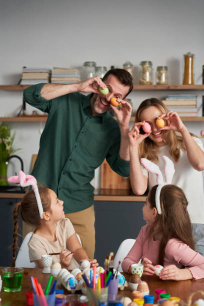 Playful caucasian family covering eyes with easter eggs and laughing stock photo