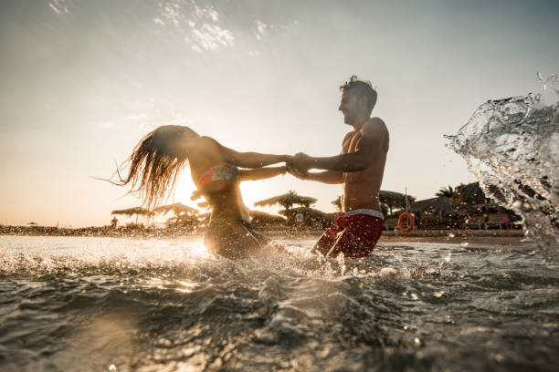 Playful couple spinning in the sea at sunset. stock photo
