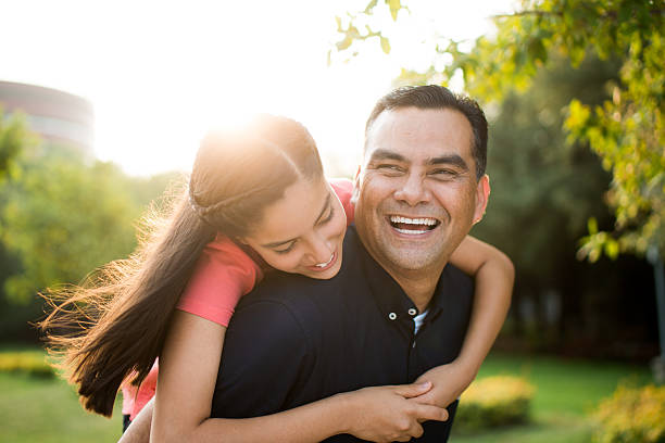 playful latin father and teen daughter laughing - hugging outside stockfoto's en -beelden