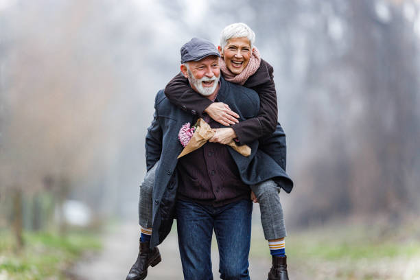 Playful mature couple piggybacking in winter day. stock photo