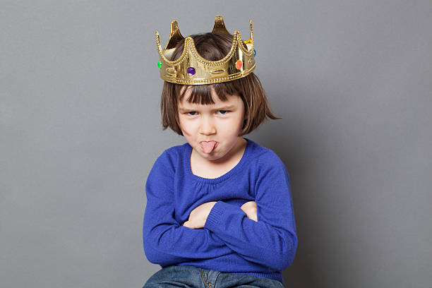 playful preschooler with cheeky attitude and mollycoddled kid crown spoiled kid concept - cheeky preschool child with golden crown on head folding arms and sticking out tongue for disrespectful mollycoddled little king or queen metaphor,studio shot brat stock pictures, royalty-free photos & images