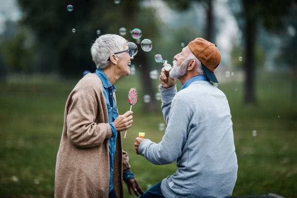 Playful senior couple blowing bubbles from bubble wand at the park. Happy mature couple having fun with bubble wand in the park. bubble wand stock pictures, royalty-free photos & images