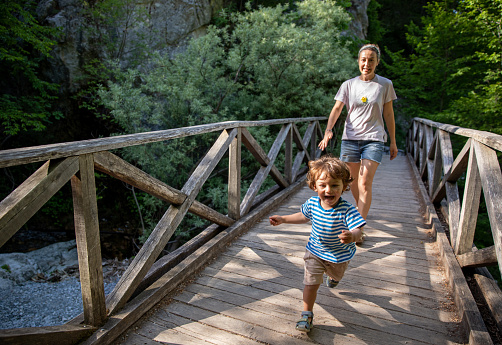 Male toddler running with her mother on wooden bridge out in nature