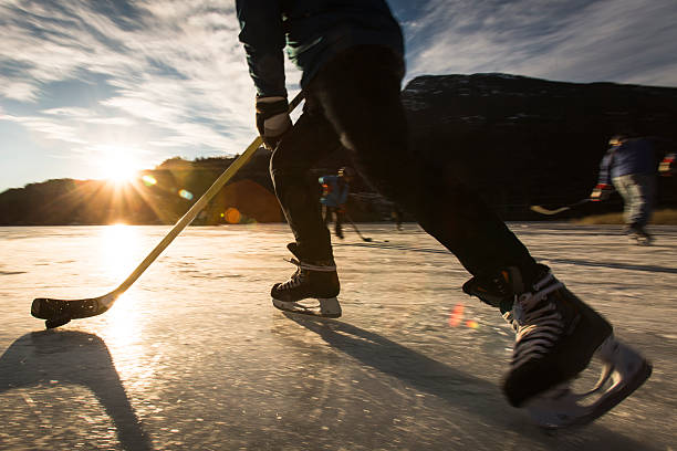 Playing ice hockey on frozen lake in sunset. stock photo