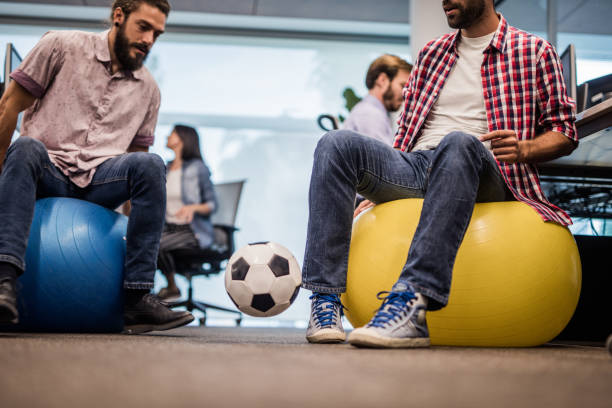Playing with soccer ball on a break in the office! Two men sitting on fitness ball in the office and having fun while playing with soccer ball. Copy space. yoga ball work stock pictures, royalty-free photos & images