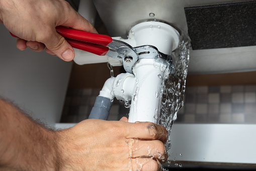 A plumber fixing a leaking sink pipe