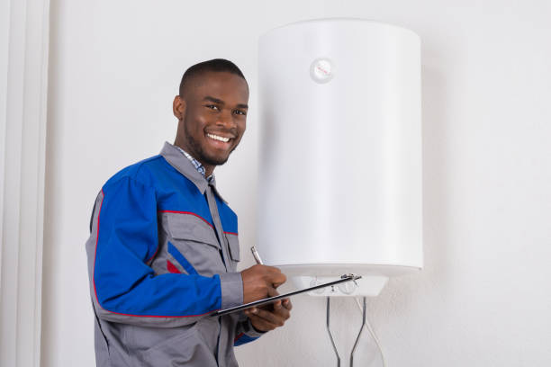 Plumber Looking At Electric Boiler Young African Male Plumber Holding Clipboard Looking At Electric Boiler african american plumber stock pictures, royalty-free photos & images