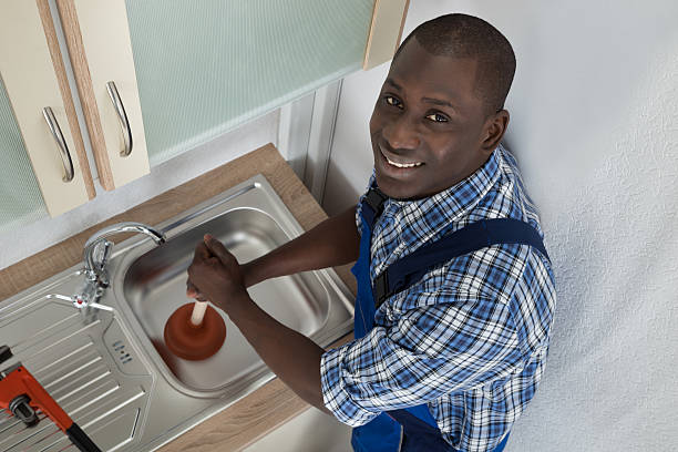 Plumber Using Plunger In Kitchen Sink Young Happy African Plumber Using Plunger To Unclog Kitchen Sink african american plumber stock pictures, royalty-free photos & images