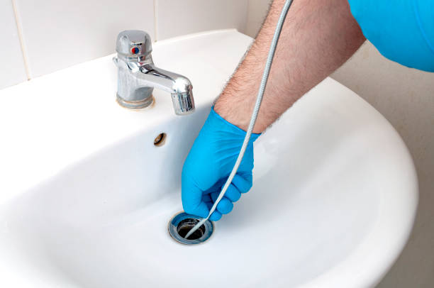 Plumbing issues, occupation in sanitation and handyman contractor concept with plumber repairing drain with plumbers snake (steel spiral that twists through pipes to collect dirt) in residential sink stock photo