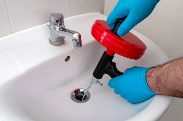 Plumbing issues, occupation in sanitation and handyman contractor concept with plumber repairing drain with plumbers snake (steel spiral that twists through pipes to collect dirt) in residential sink stock photo