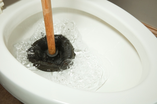 A rubber plunger is working on a toilet clog and displacing water.