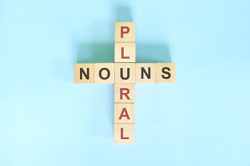 Plural Nouns concept in English grammar noun education. Wooden block crossword puzzle flat lay in blue background.