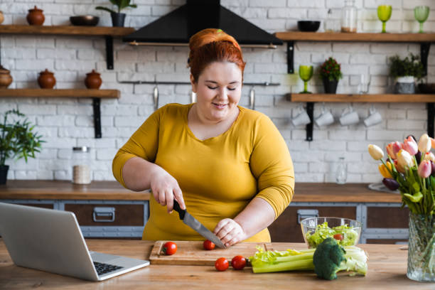 플러스 크기, 소셜 미디어에서 샐러드와 건강한 음식을 만드는 법을 배우는 백인 여성, 소셜 멀리, 홈 컨셉에 머물 - 무거운 뉴스 사진 이미지