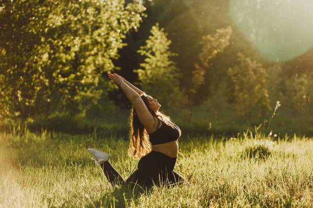 Plus size girl doing yoga in nature. Beautiful plus size girl doing yoga in nature on a sunny summer day. Body positive, sports for women, harmony, asana, healthy lifestyle, inspiring look, self-love and wellness. voluptuous women images stock pictures, royalty-free photos & images