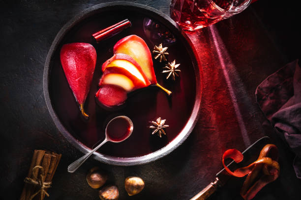Poached pears in red wine recipe sliced served on dark plate Poached pears in red wine recipe sliced served on dark plate with cinnamon and citrus peel, ingredients moody light and res wine light beams chiaroscuro stock pictures, royalty-free photos & images
