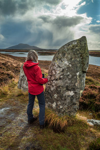 Pobull Fhinn Standing Stone on North Uist, Scotland Woman beside Pobull Fhinn Standing Stone on North Uist, part of the Outer Hebrides of Scotland. Mountain called Eabhal in the distance over Loch Langais. megalith stock pictures, royalty-free photos & images