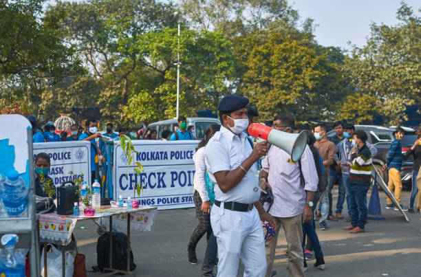 Police alertness near Victoria Memorial of Kolkata on the first day of 2021 Kolkata,01/01/2021: Standing among crowd of visitors near the entrance of Victoria Memorial garden, a white uniformed Kolkata police-person announcing covid-19 safety protocols with a megaphone, advising visitors to mandatorily wear face mask and to maintain safe distancing. A police checkpoint is seen in background. kolkata stock pictures, royalty-free photos & images
