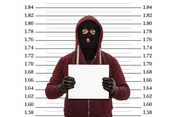 Police lineup or mug shot concept with a burglar or thief wearing a ski mask or balaclava and holding a blank white cardboard with copy space against a metric size chart with clipping path Police lineup or mugshot concept with a burglar or thief wearing a ski mask or balaclava and holding a blank white cardboard with copy space against a metric size chart with clipping path ski mask criminal stock pictures, royalty-free photos & images