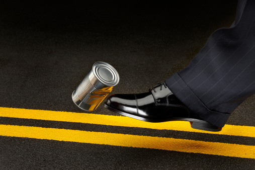 close up of politician's shoe kicking a dented shiny can down the road