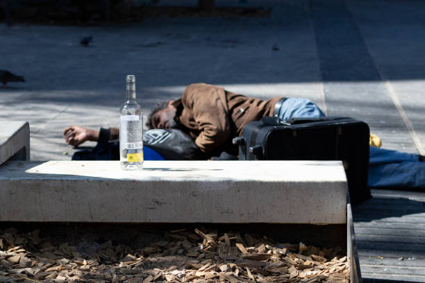 Poor homeless drunk man sleeping on the floor of the street on the background an empty bottle of wine. Barcelona, Catalonia, Spain 2019-04-30 stock photo