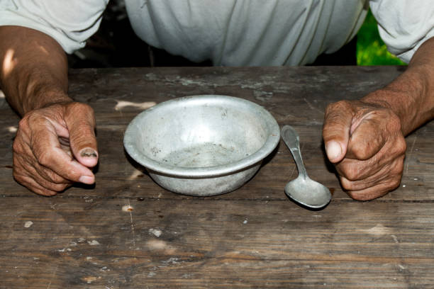 Poor old man's hands and empty bowl on wooden background.An angry hungry man clenches his hands into fists. the concept of hunger or poverty. Selective focus.Homeless. Alms stock photo