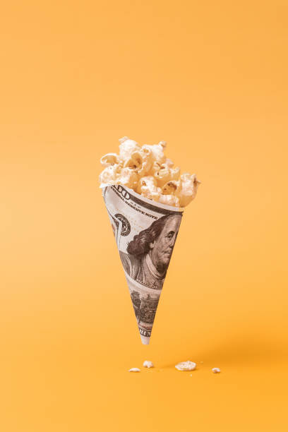 Popcorn in a cone of dollar bills on yellow monochrome background stock photo