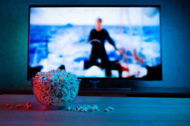 Popcorn in a glass plate on the background of the TV. Color bright lighting, blue and red. Background Popcorn in a glass plate on the background of the TV. Color bright lighting, blue and red. Background watching tv stock pictures, royalty-free photos & images