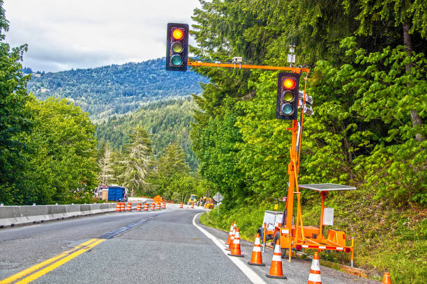 Portable solar powered traffic light at construction site in tree covered mountains with equipment and traffic cones stock photo