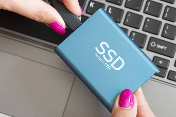 Portable SSD state solid drives disk in woman’s hands against notebook keyboard stock photo