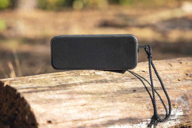 Portable wireless bluetooth speaker for listening to music on a log in the forest stock photo