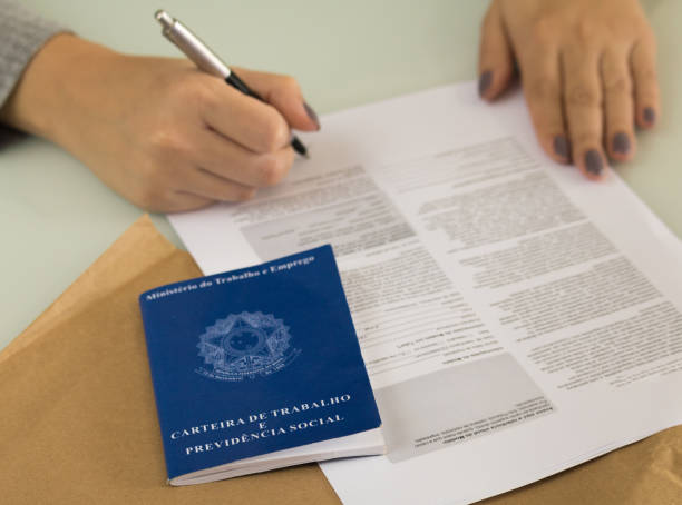 A portfolio of Brazilian workers (Translation "Work Permit, Ministry of Labor and Social Security Brazil CTPS"), female hand signing a work contract background. stock photo