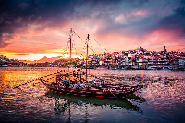 Porto at Sunset with Rabelo Boats on Douro River and the city in the background. The sky is coloured and the boats are in the foreground.