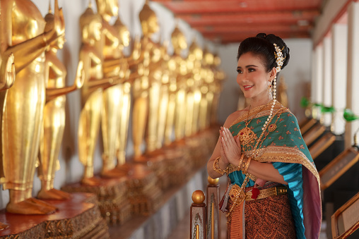 Portrait Asian women smiling and wearing Thai national costumes are inside temples to worship Buddha with flower garlands on important religious days for Thai people.