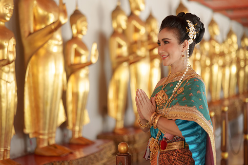 Portrait Asian women smiling and wearing Thai national costumes are inside temples to worship Buddha with flower garlands on important religious days for Thai people.
