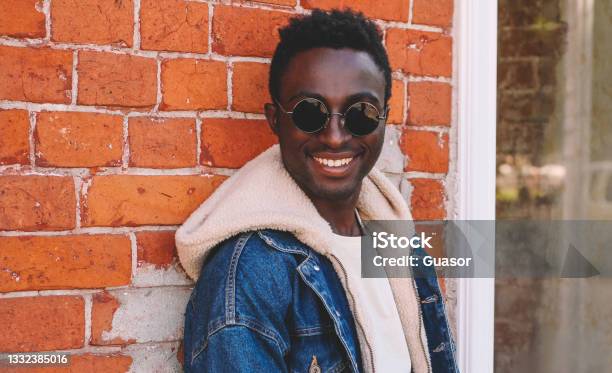 Portrait close up of modern stylish happy smiling young african man on a city street over brick background