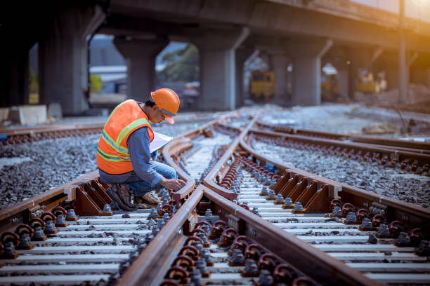 ポートレートエンジニアは、建設プロセスの線路スイッチを点検し、チェックし、鉄道駅での作業をチェックしています。安全服と安全ヘルメットを着用したエンジニア。 - 電車 ストックフォトと画像