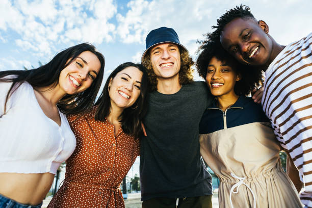 Portrait group of young happy multiracial people standing outdoors in a sunny day - Cheerful multicultural friends embracing in the street - Community and unity concept stock photo