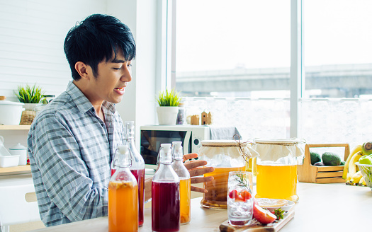 Portrait handsome man smiling with fresh and happiness, recommending Kombucha healthy fermented probiotic tea drinks with ingredients red apples, strawberries, mushroom scoby in kitchen at home