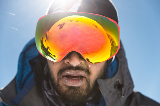 A portrait of a bearded man wearing ski goggles on his way to the top of the mountain. The concept of endurance in the way